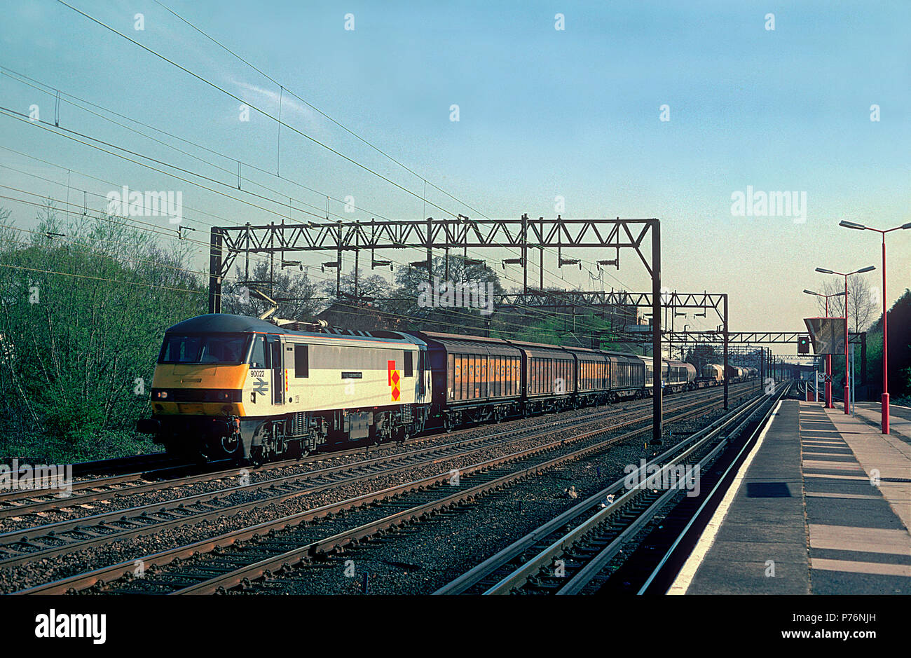 A class 90 electric locomotive number 90022 ‘Freightconnection’ heads north along the West Coast Main Line with a lengthy Railfright Distribution wagonload freight at South Kenton. 11th April 1994. Stock Photo