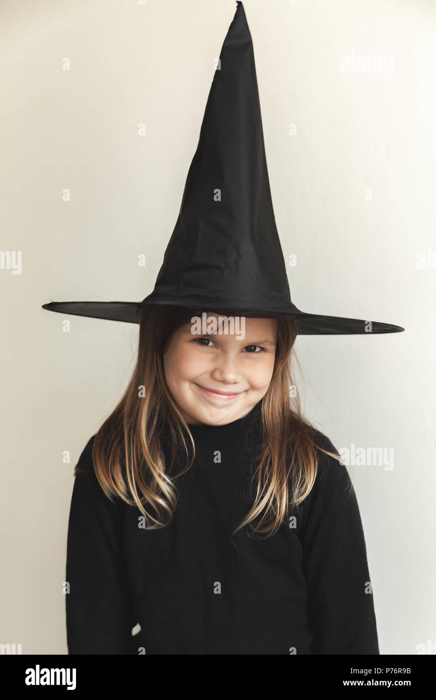 Smiling little blond girl in black witch costume over white wall, close-up studio portrait Stock Photo