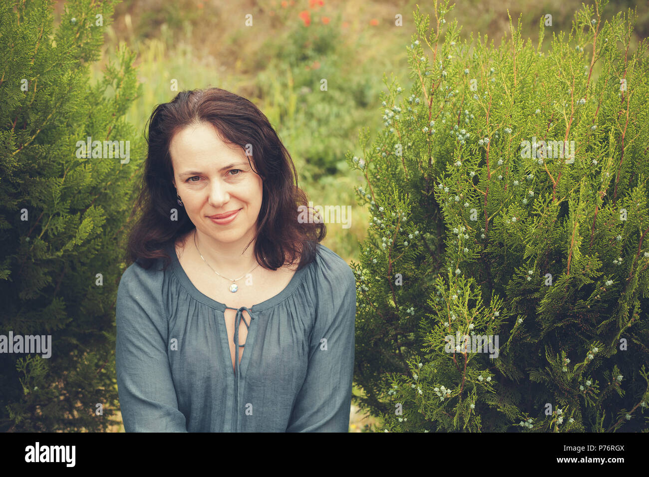 Smiling young adult European woman in garden. Vintage toned outdoor portrait Stock Photo