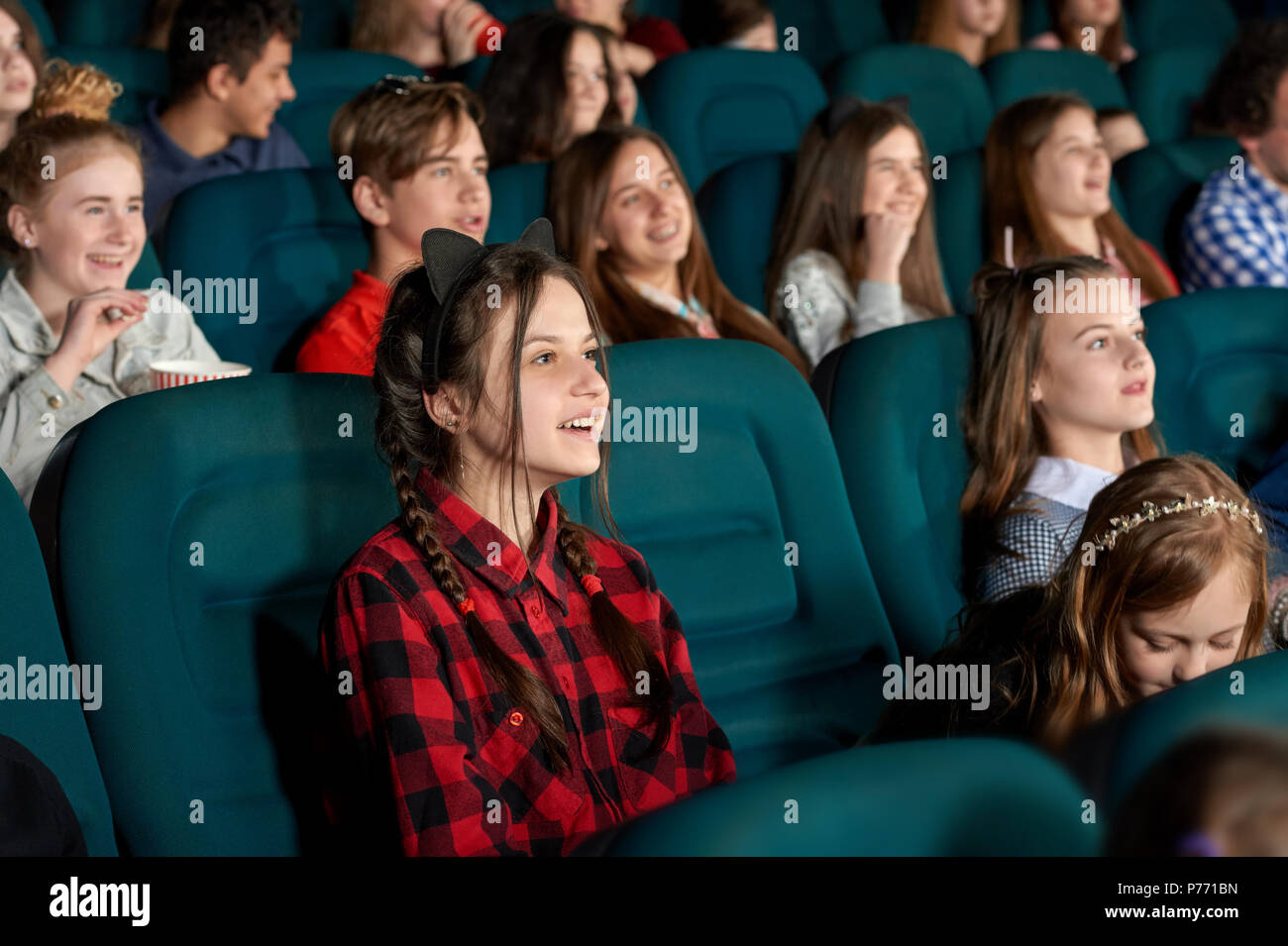 Beautiful young girl watching film with steadfast eyes and smiling, expressing facial emotions. Youth having fun, sitting in comfortable chairs in mod Stock Photo