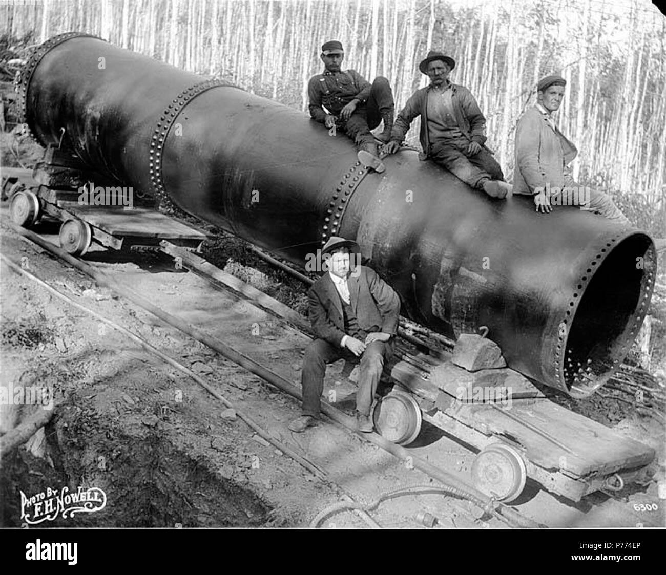 English: Men sitting on large pipe section, Alaska (), n.d. English:  Caption on image: Photo by F.H. Nowell, 6300 Subjects (LCTGM): Pipes  (Conduits)--Alaska; Group portraits . Unknown date 9 Men sitting