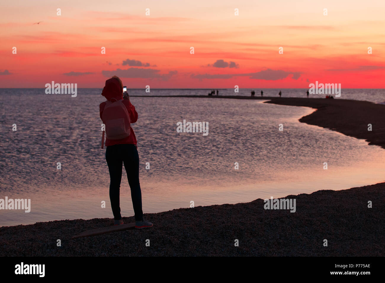 Woman traveler using smartphone and taking photo of colorful sea sunset. Stock Photo