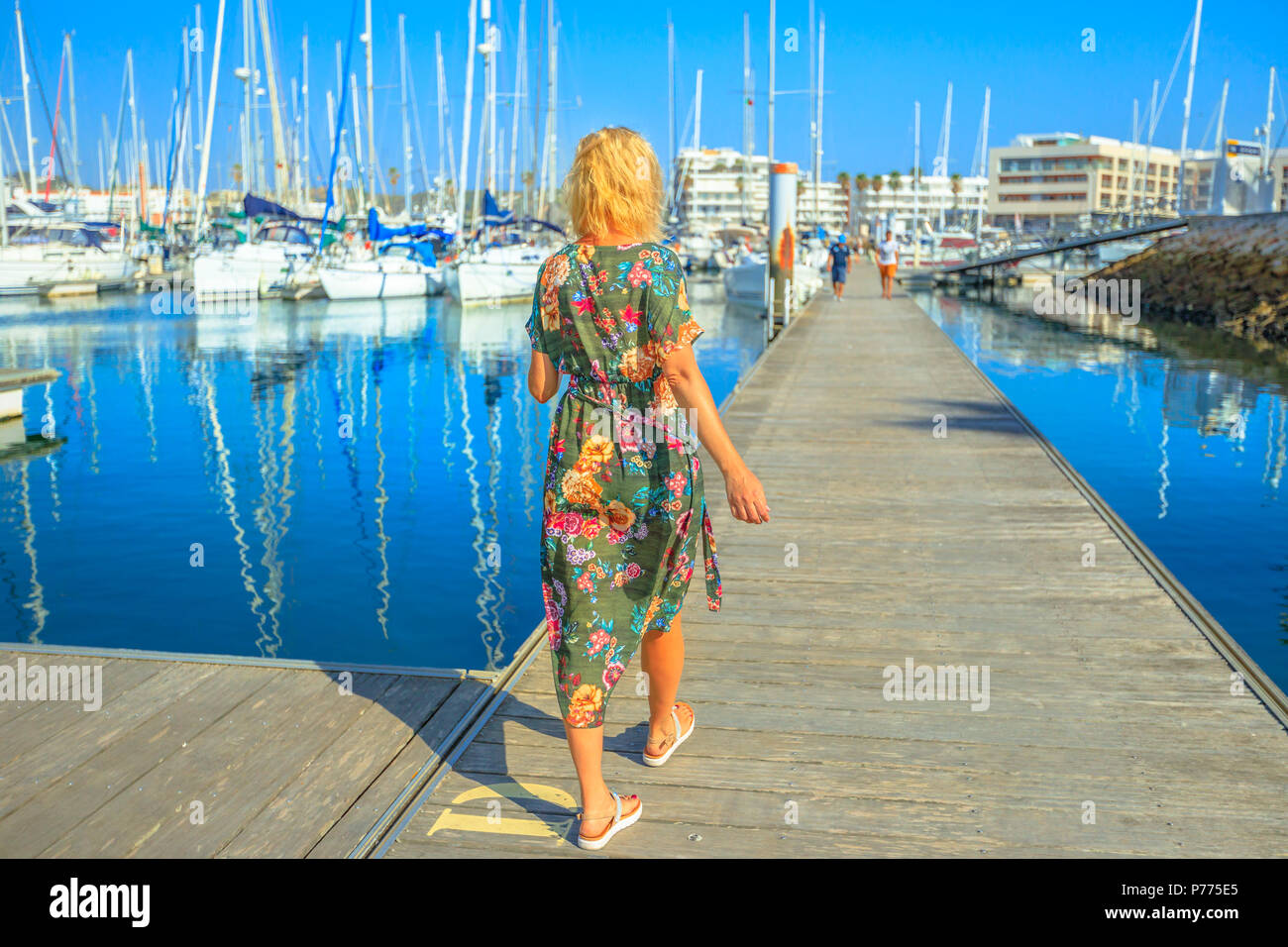 Tourism in Portugal. Lifestyle female tourist walking on wooden jetty at Marina de Lagos on Algarve coast, Portugal, Europe. Caucasian woman at Bay of Lagos in summer holidays. Stock Photo