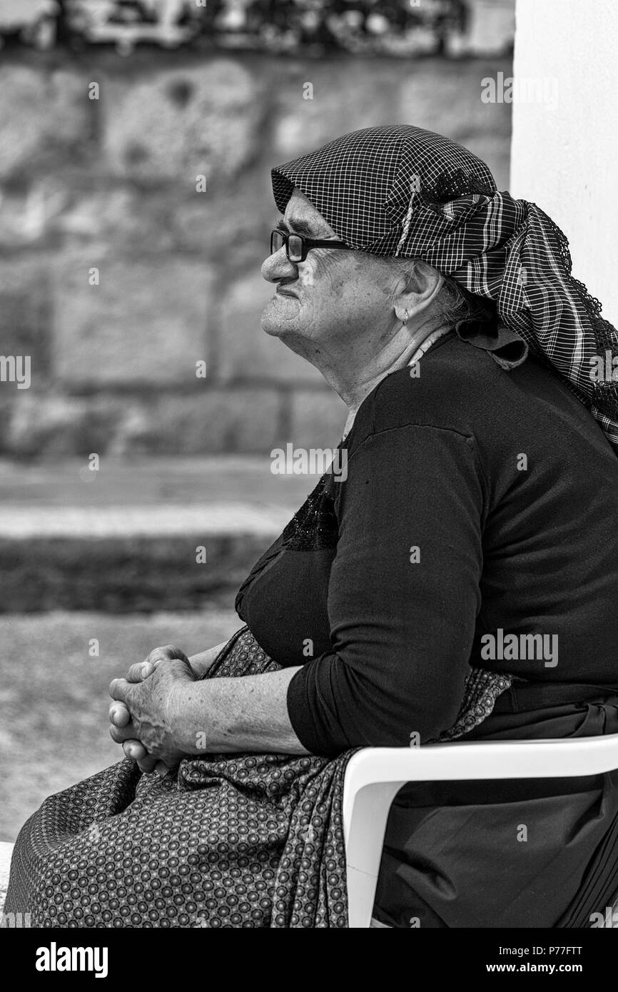 Old lady sits in the central square called Trg Svetog Stjepana outside the cathedral, Hvar, Split-Dalmatia, Croatia.  Black and white version. Stock Photo