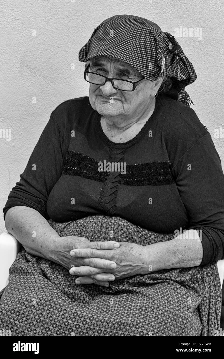 Old lady sits in the central square called Trg Svetog Stjepana outside the cathedral, Hvar, Split-Dalmatia, Croatia.  Black and white version. Stock Photo