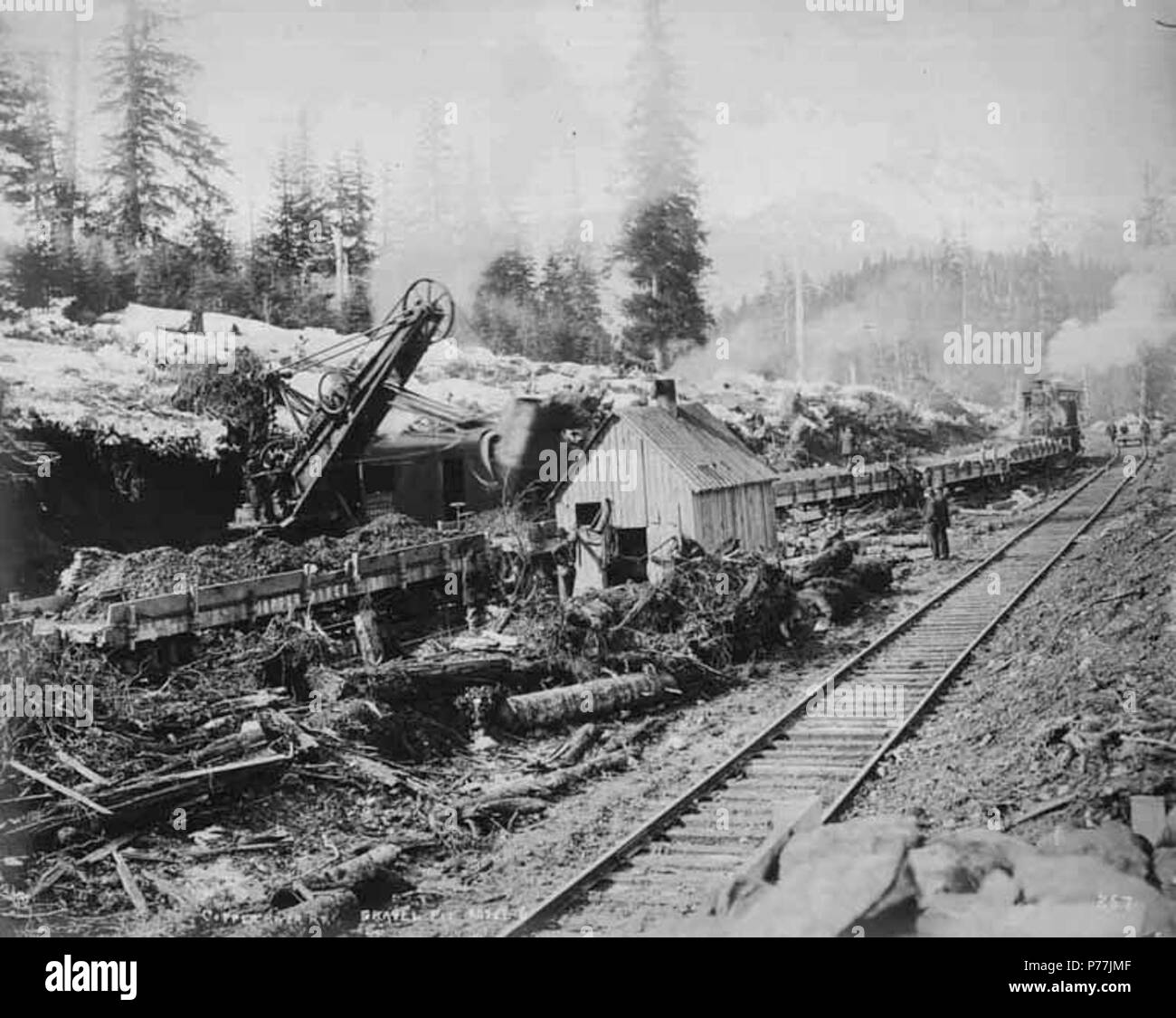 . English: Steam shovel working at the gravel pit at Mile 6 showing railroad tracks and locomotive in the background, vicinity of Eyak, 1908 . English: Construction photographs of the Copper River and Northwestern Railway along the Copper River from 1906-1911. Caption on image: E.A. Hegg 257. Copper River Ry. Gravel Pit. Mile 6 PH Coll 375.32 Subjects (LCTGM): Railroad construction & maintenance--Alaska; Steam shovels; Railroad tracks--Alaska Subjects (LCSH): Gravel--Alaska  . 1908 12 Steam shovel working at the gravel pit at Mile 6 showing railroad tracks and locomotive in the background, vic Stock Photo