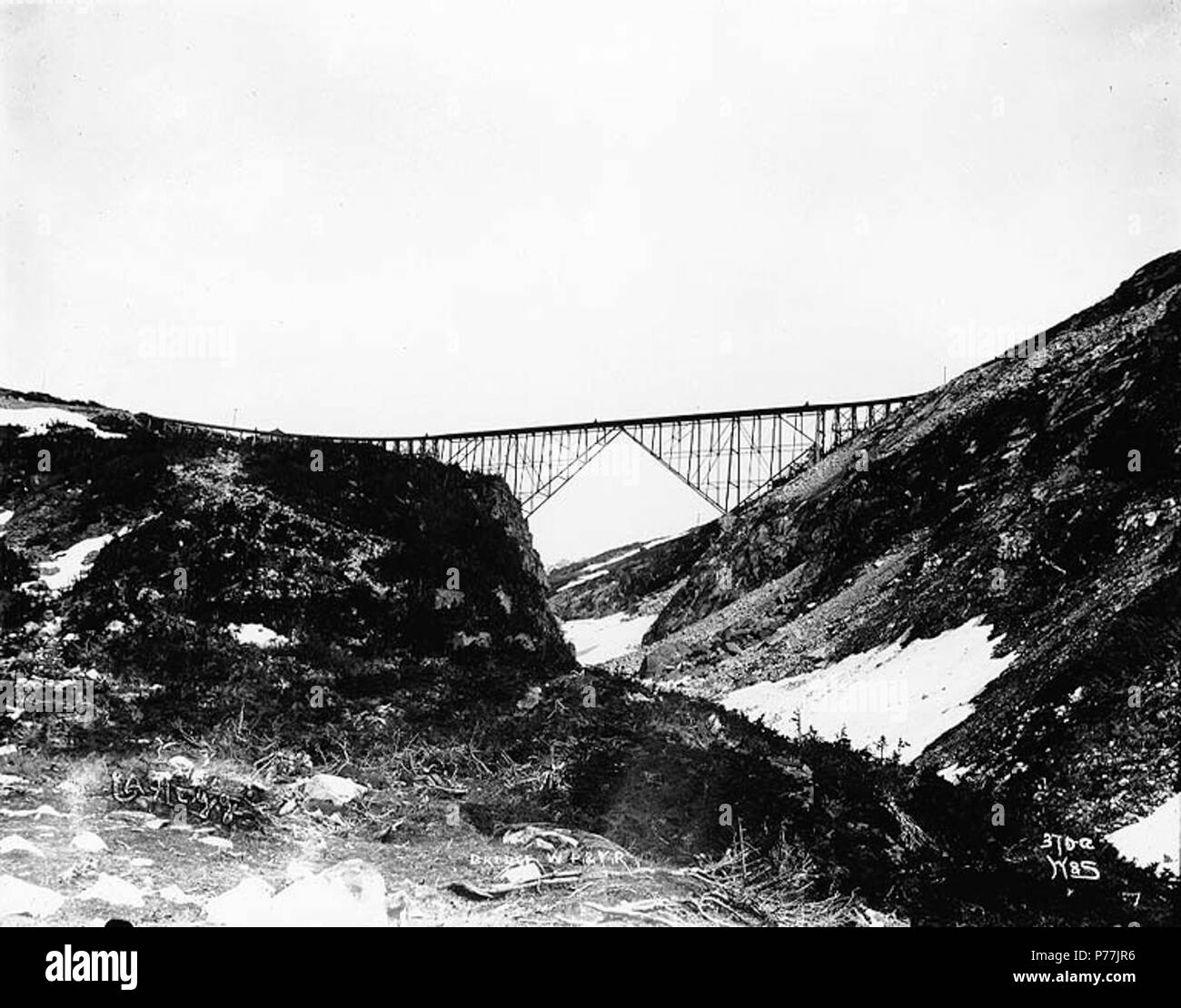 . English: Steel arch bridge spanning Dead Horse Gulch near the summit of White Pass on the White Pass and Yukon Railroad, Alaska, ca. 1901 . English: Caption on image: 'Bridge W.P. & Y.R.' Original image in Hegg Album 3, page 1 . Original photograph by Eric A. Hegg 824; copied by Webster and Stevens 370.A. Subjects (LCTGM): Railroad bridges--Alaska--Dead Horse Gulch; Canyons--Alaska Subjects (LCSH): White Pass & Yukon Route (Firm); Dead Horse Gulch (Alaska)  . circa 1901 12 Steel arch bridge spanning Dead Horse Gulch near the summit of White Pass on the White Pass and Yukon Railroad, Alaska,  Stock Photo