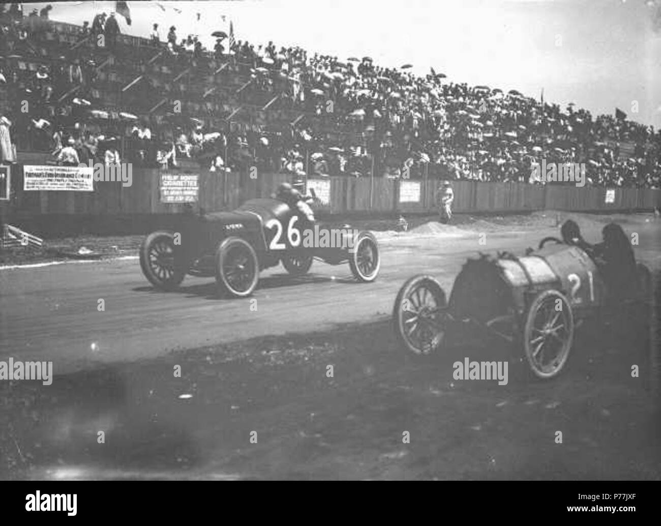 English: Car #26, driven by N. Latta, and car #21, believed to be a Studebaker driven by H. Staley, drive past the grandstand of the Tacoma Speedway. This race is believed to be the July 1914 InterCity 100-mile race held at the Tacoma Speedway which featured cars from cities in the Pacific Northwest. Driver Latta, from Seattle, drove the #26 Lozier which came in third place in the race. The News Tribune noted that Latta did not pit or stop on the racetrack before crossing the finish line. Latta won $250 and Staley, the 4th place winner, earned $150 for the race. Jim Parsons, also of Seattle, w Stock Photo