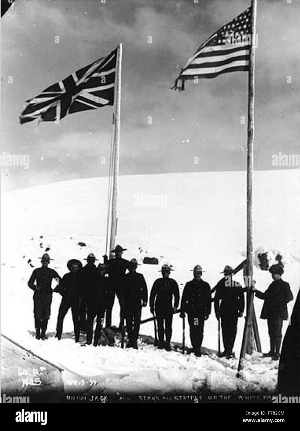 . English: North-West Mounted Police standing next to American and British flags marking the boundary between Alaska and British Columbia, White Pass, April 9, 1899. English: Caption on image: 'Union Jack, and Stars and Stripes on the White Pass Apr 9 '99'' Original photograph by Eric A. Hegg 540; copied by Webster and Stevens 60.A. Subjects (LCTGM): Mounted police; North West Mounted Police (Canada) Subjects (LCSH): Flags--American; Flags--British; Mountain passes  . 9 April 1899 10 North-West Mounted Police standing next to American and British flags marking the boundary between Alaska and B Stock Photo