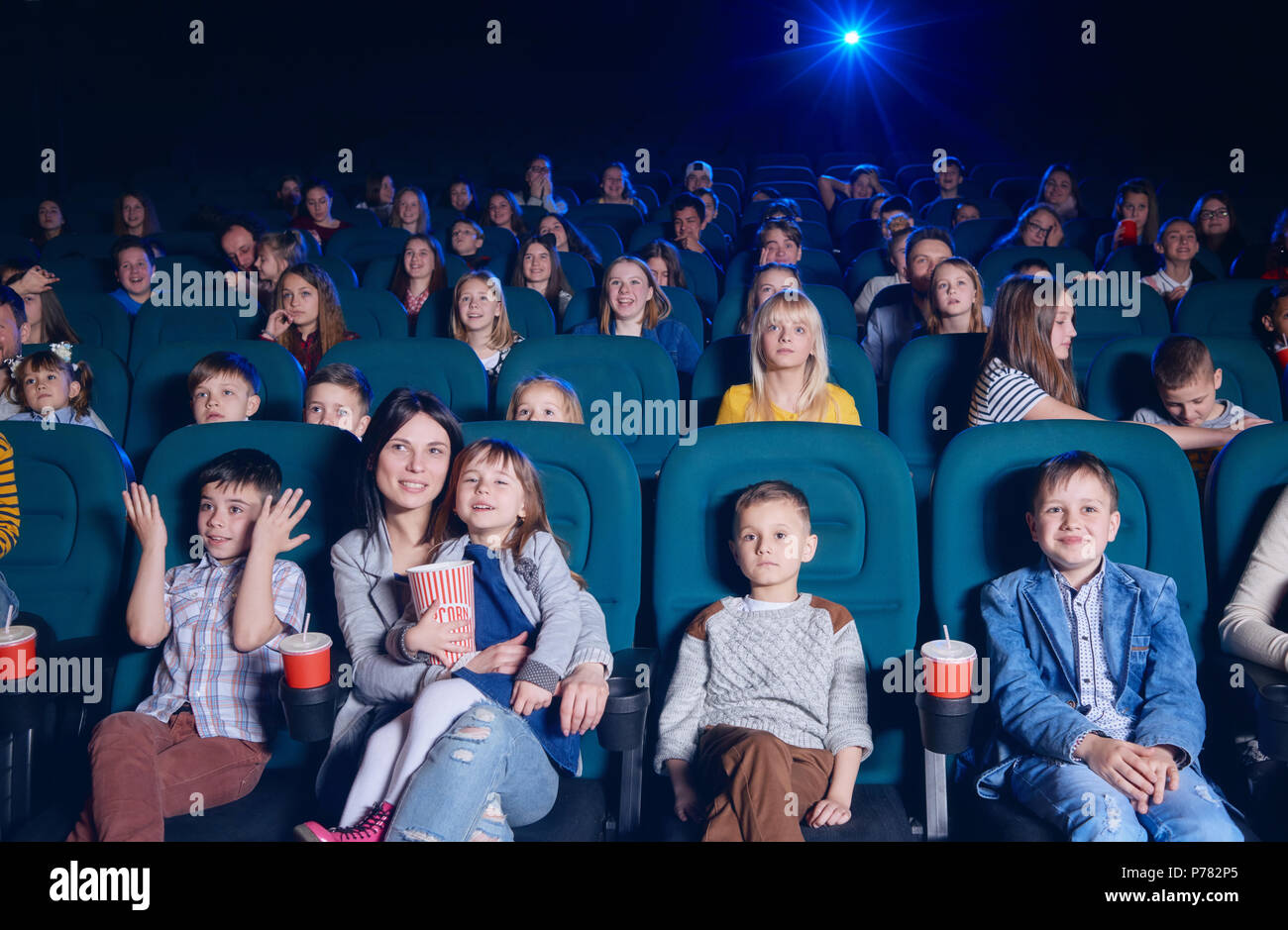 View of group of young people sitting in movie theatre, expressing emotions on their faces while watching film. Young spectators having fun, smiling.  Stock Photo
