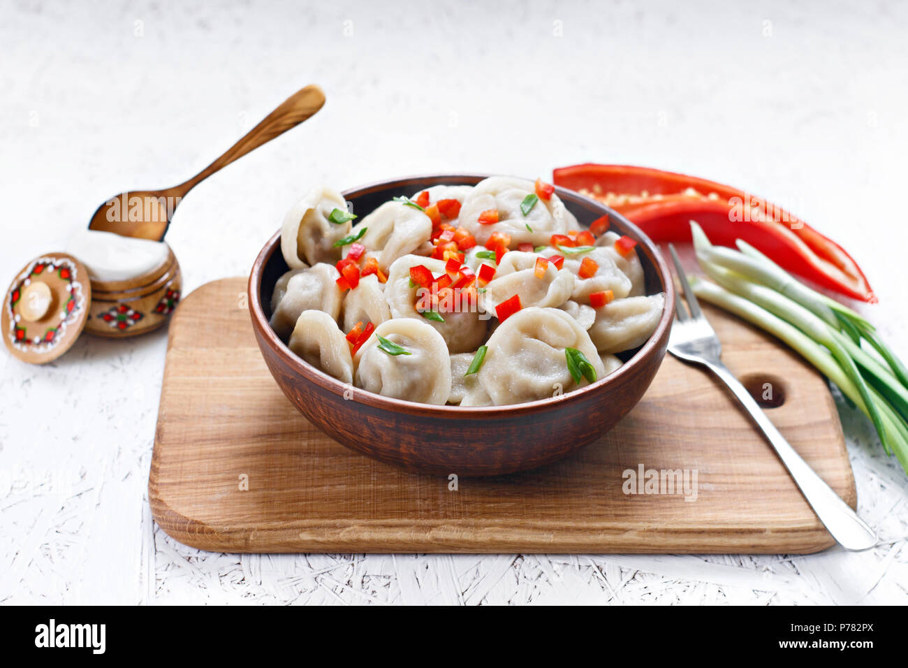 Cooked dumplings in a clay dish with pepper and onions on a wooden board. Stock Photo