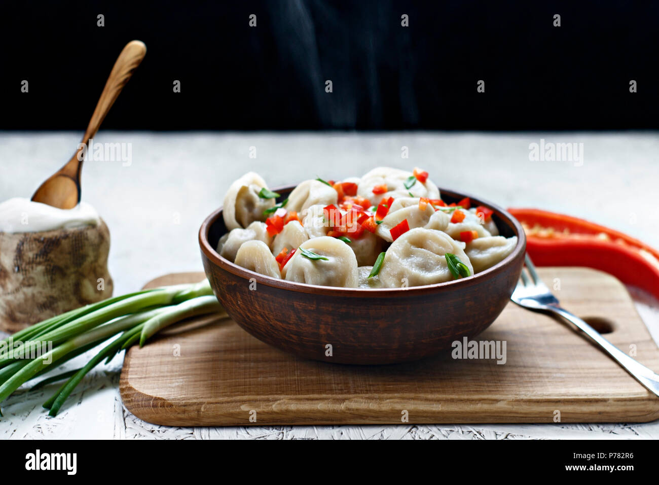 Cooked dumplings in a clay dish with pepper and onions on a wooden board. Stock Photo