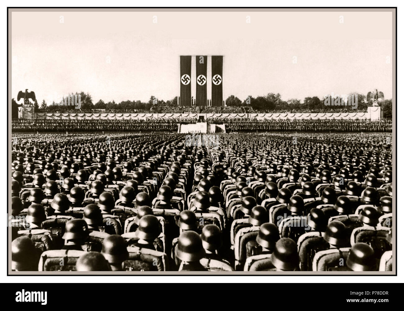 Nuremberg 1930's Waffen SS troops wearing polished helmets in precise serried ranks standing at salute during a German Nazi rally pre-World War II with large Swastika banners dominating arena Stock Photo