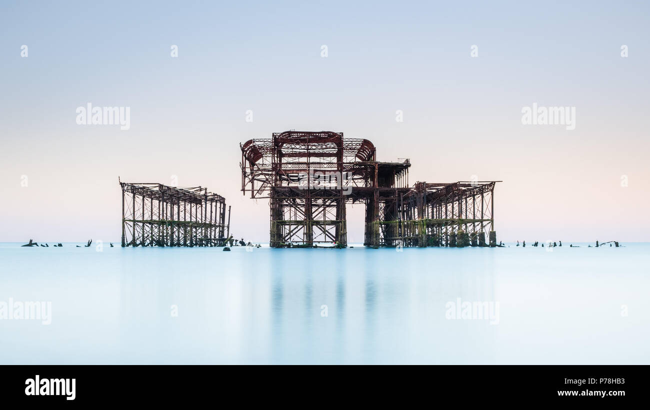 Minimalistic West Pier in Brighton, East Sussex, at sunrise and reflected in a calm sea with beautiful pastel shades in a cloudless sky Stock Photo