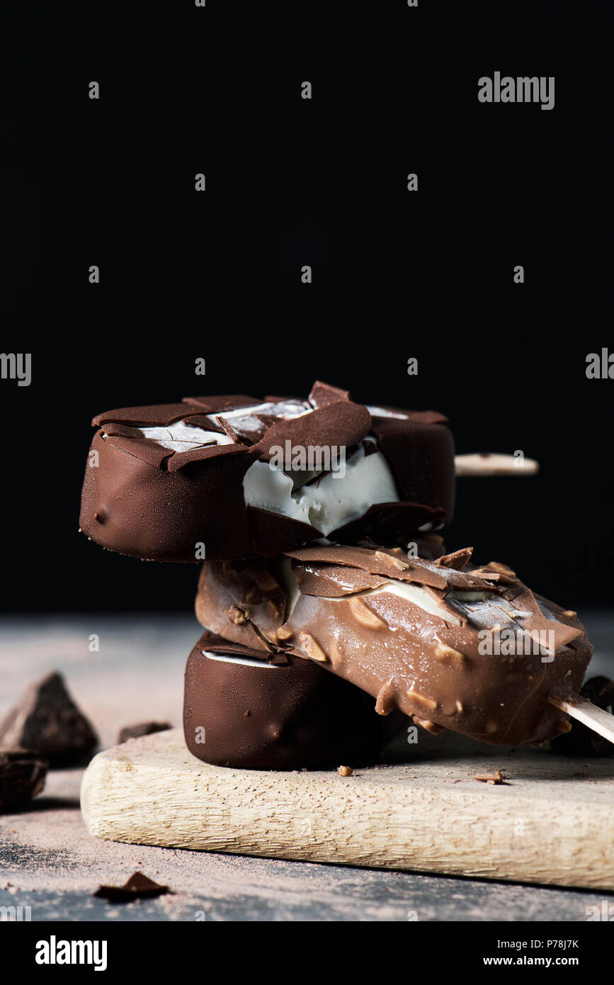 closeup of some chocolate ice cream bars on a chopping board, placed on a dark rustic wooden table, against a black background with some blank space o Stock Photo