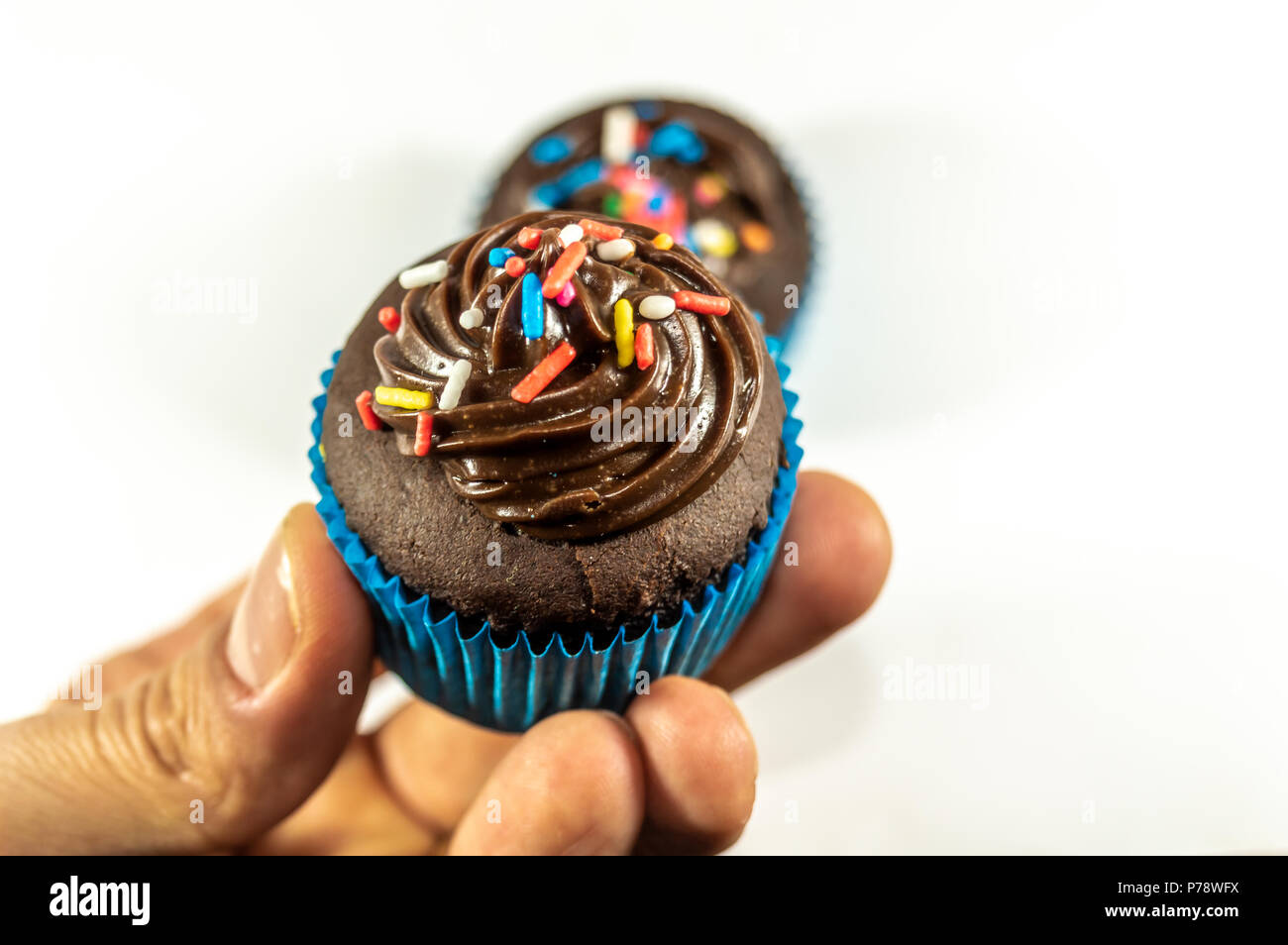 Personal perspective of a person holding a chocolate cupcake isolated on white background Stock Photo