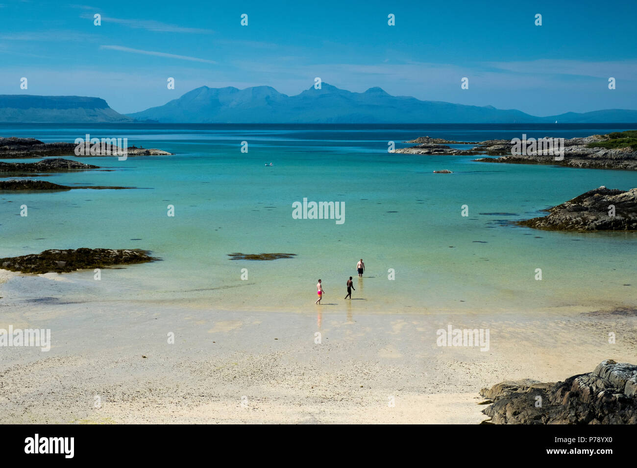 Swimmers in the sea in a sandy bay at Traigh near Arisaig with the islands of Eigg and Rum in the distance. Stock Photo