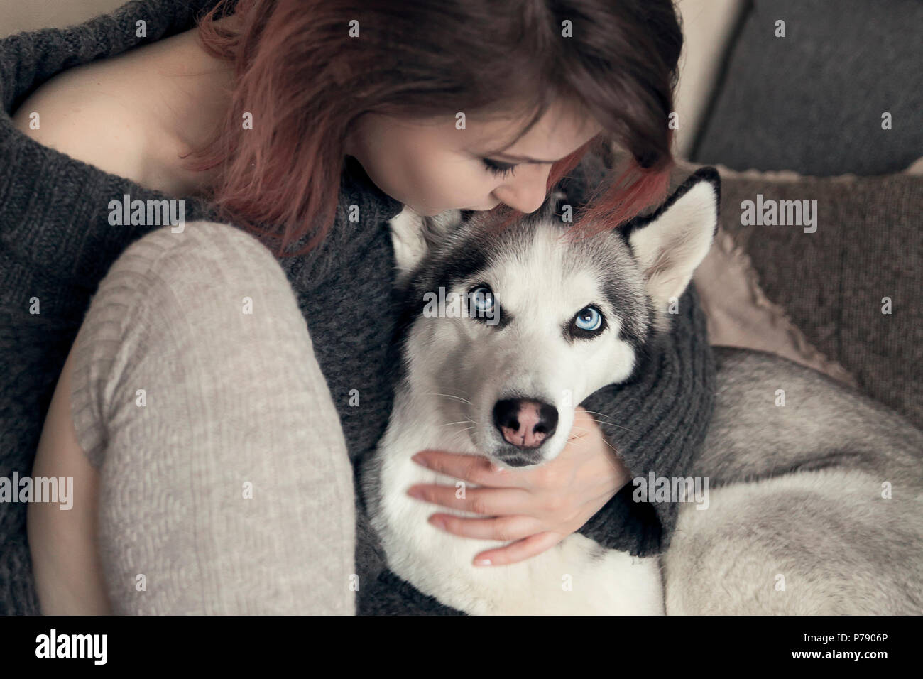 Young woman in cozy warm winter clothes, stroking her husky dog Stock Photo