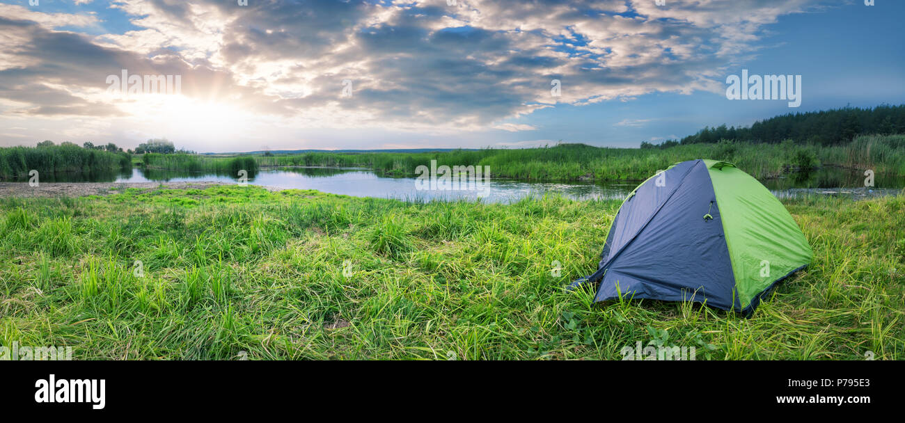Green and gray tourist tent on the river bank in summer Stock Photo