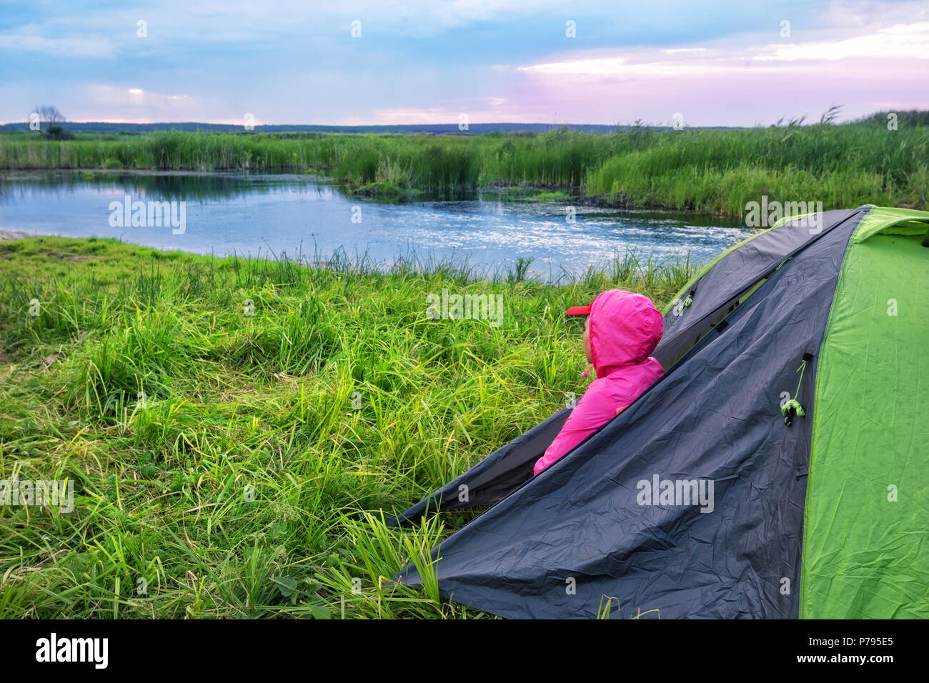 Woman in a pink jacket with hood looks out of the tent at dawn o Stock Photo
