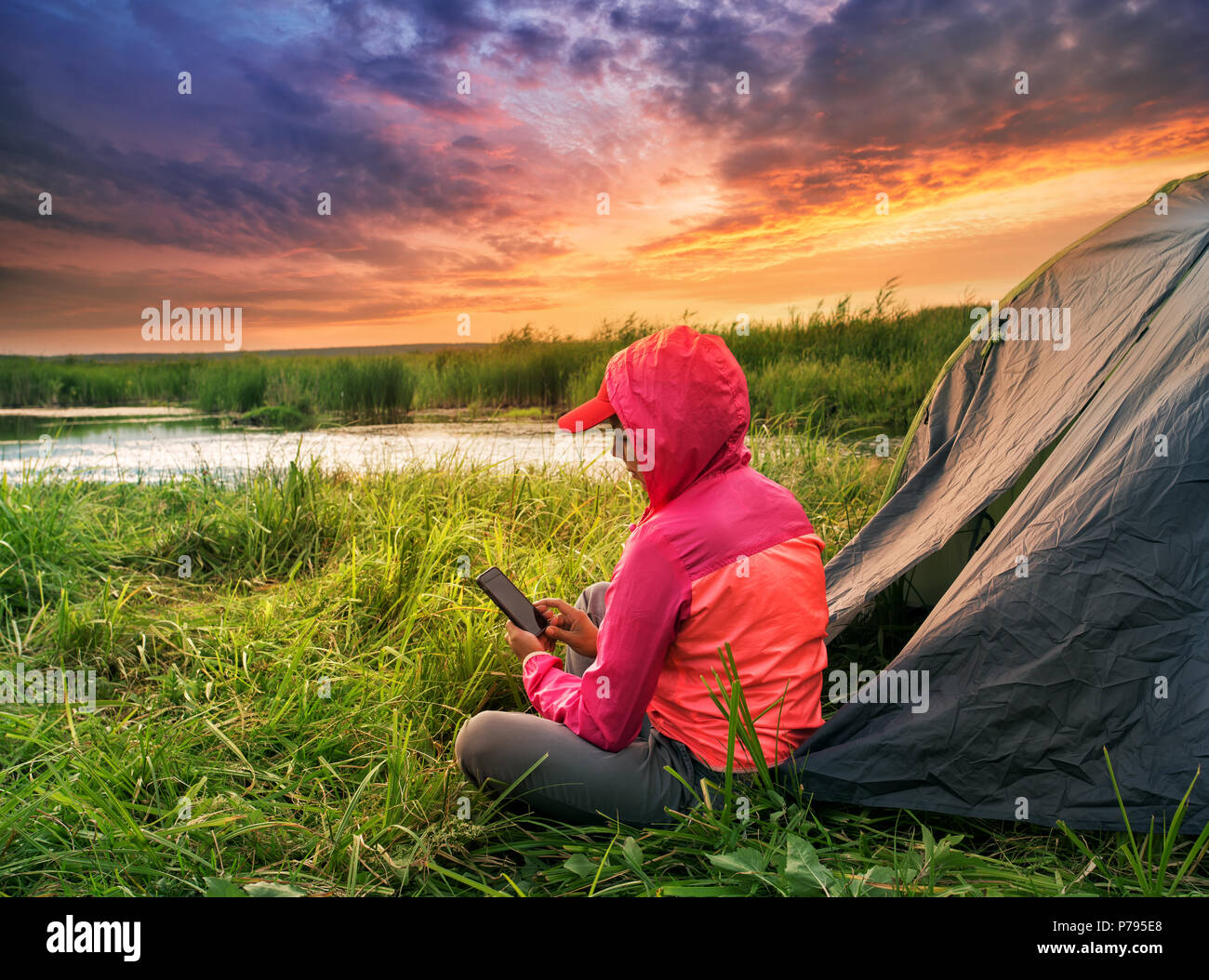 Woman in pink jacket is sitting with mobile phone near the tent Stock Photo