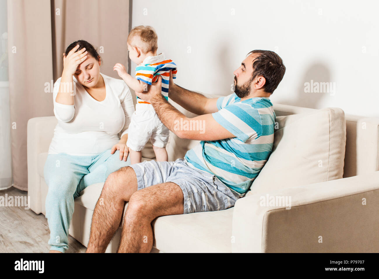 A man and a woman with a small child are sitting on the sofa in the room. Stock Photo
