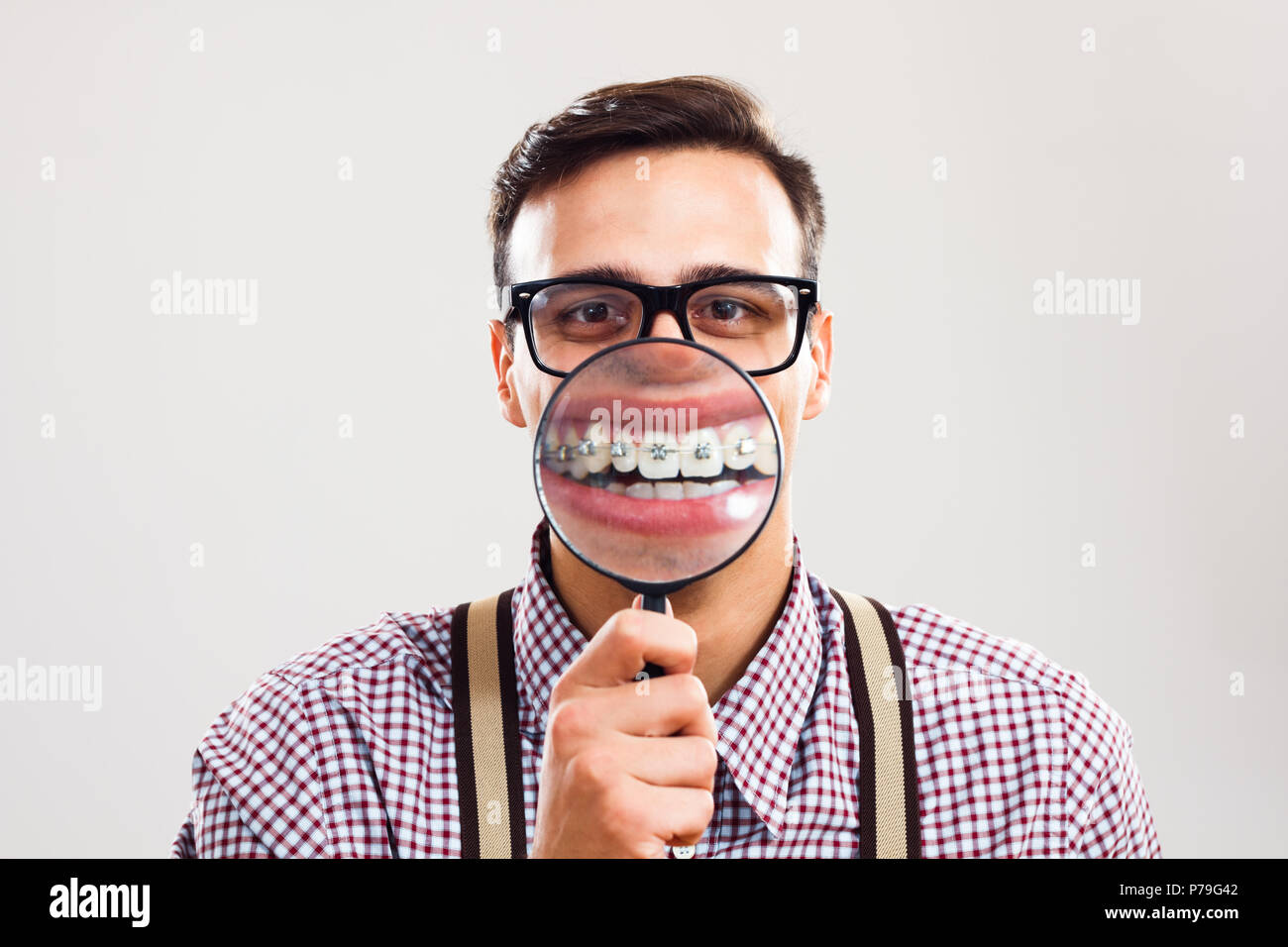 Nerdy man is showing his braces with magnifying glass Stock Photo - Alamy