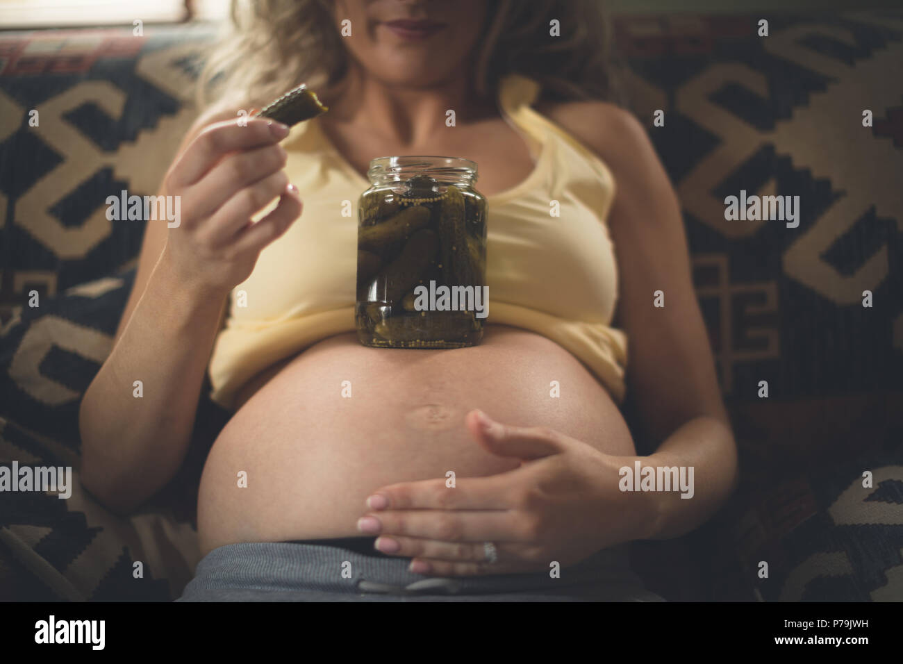 Pregnant woman having pickle in living room Stock Photo