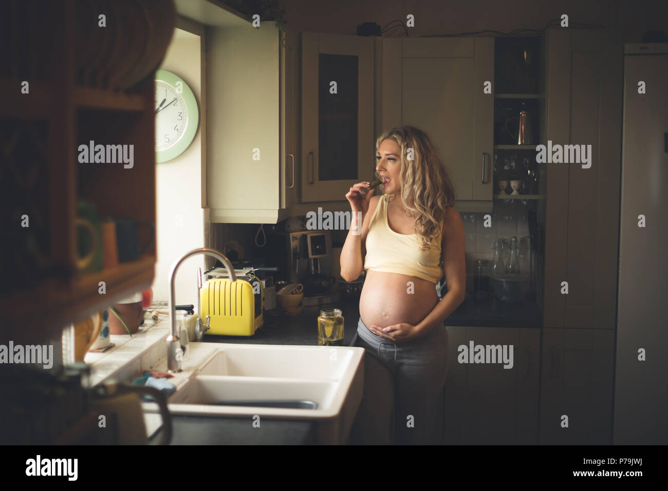 Pregnant woman having pickle in kitchen Stock Photo