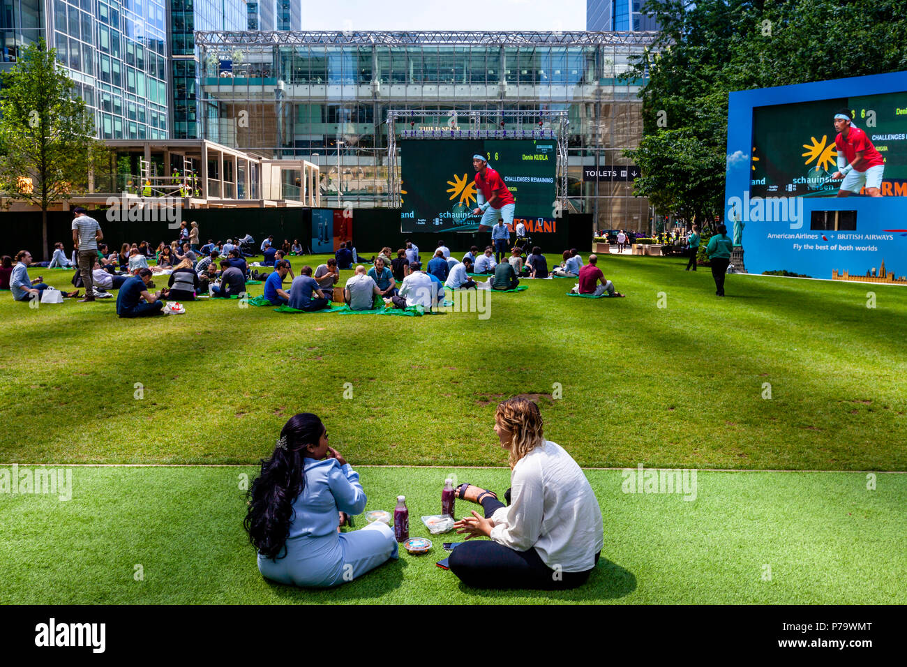 Office Workers Sitting On The Grass Eating Lunch, Canary Wharf, London