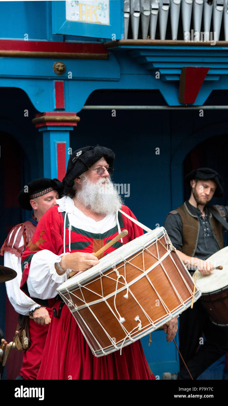 Drummer and group performing with drums at the Renaissance Festival, Maryland. The large drum hangs from the neck of Medieval reenactor in red outfit. Stock Photo