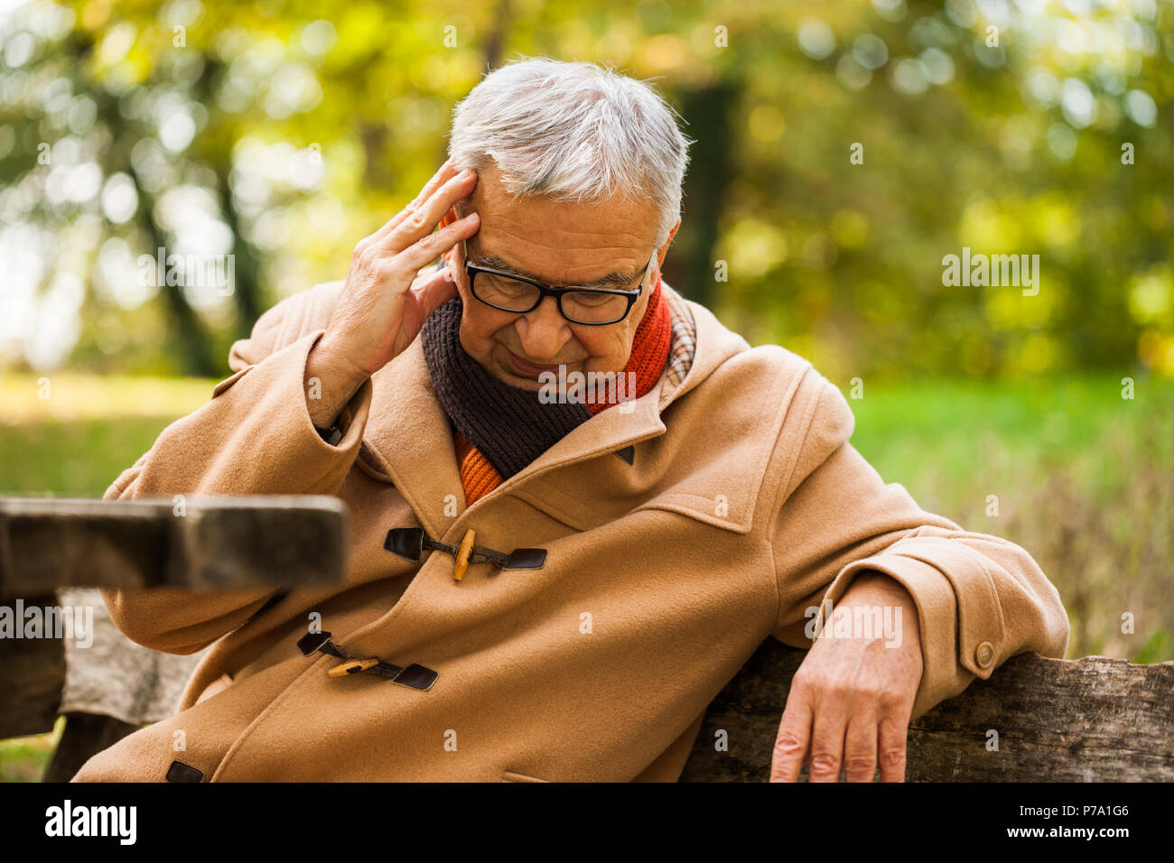 Senior man sitting in park and having headache. Stock Photo