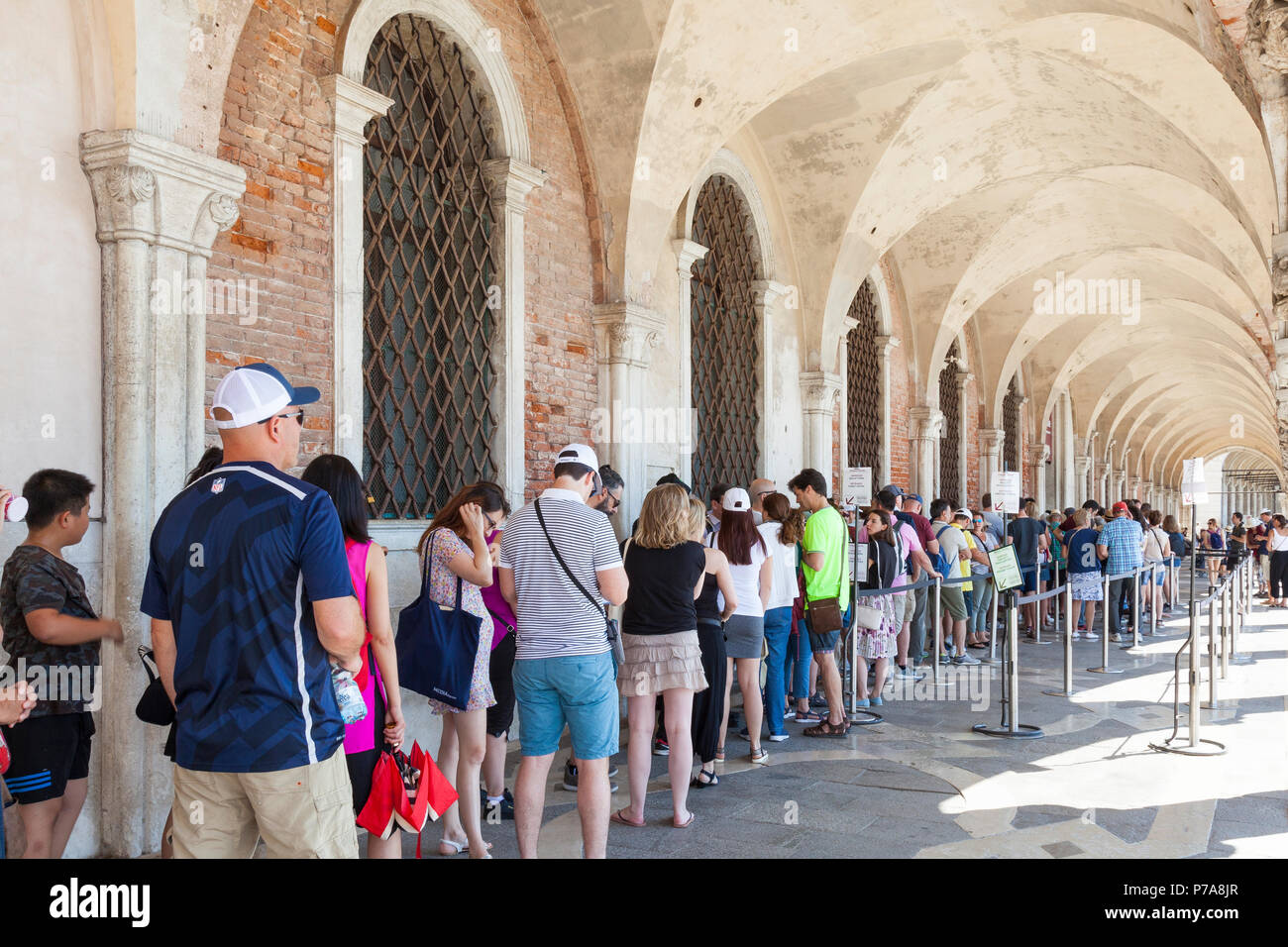 Long line of tourists queueing to enter the Doges Palace or Palazzo Ducale, San Marco, Venice, Veneto, Italy under the vaulted colonnade outside. Stock Photo