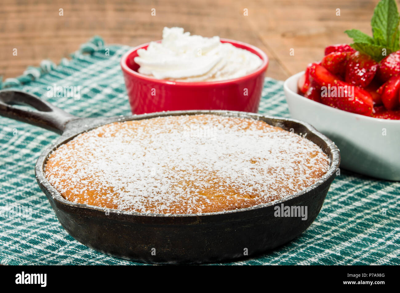 Cast iron skillet baked cake with bowl of red strawberries Stock Photo