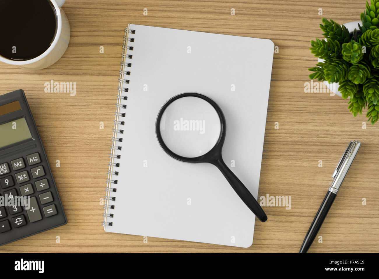 Magnifying glass on top of notebook with multiple office supply. Stock Photo