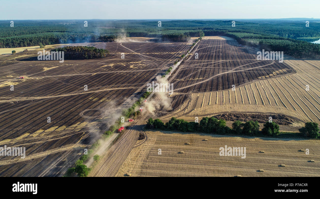 Germany, Limsdorf. 4th July, 2018. Fire department cars drive by a burned-out field. The fire which caught on some 100 hectars of forest and field land was put out over night on Thursday. More than 13 hours were needed to quench the fire in the district of Limsdorf, as the fire department reported. The police is yet unable to provide a source for the fire outbreak. Brandenburg is currently at its highest risk for forest fires. Credit: Patrick Pleul/dpa-Zentralbild/dpa/Alamy Live News Stock Photo