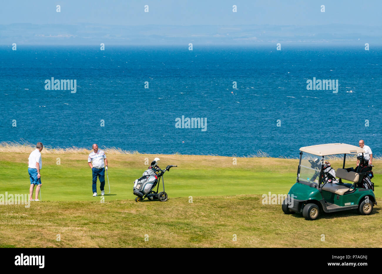 North Berwick, East Lothian, Scotland, United Kingdom, 5th July 2018.  Golfers with a golf buggy playing on Glen Golf Course beside the Firth of Forth Stock Photo
