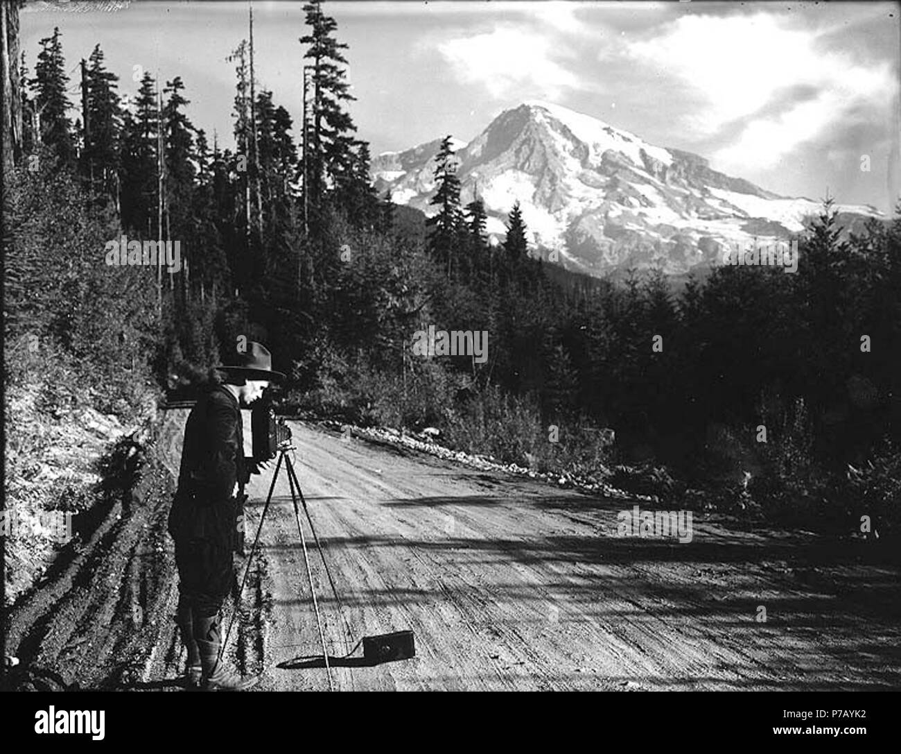 . English: Man with camera and tripod photographing views in Mount Rainier National Park, Washington, ca. 1907. English: Made for an Eastman Co. advertisement On sleeve of negative: Mt. Tacoma. Longmire. Man photographing on road showing summit for Kodak ad. Subjects (LCTGM): Mountains--Washington (State)--Mount Rainier National Park; Roads--Washington (State)--Mount Rainier National Park; Photographic apparatus & supplies; Advertising--Washington (State)--Mount Rainier National Park Subjects (LCSH): Rainier, Mount (Wash.); Kodak camera; Mount Rainier National Park (Wash.)  . circa 1907 54 Man Stock Photo