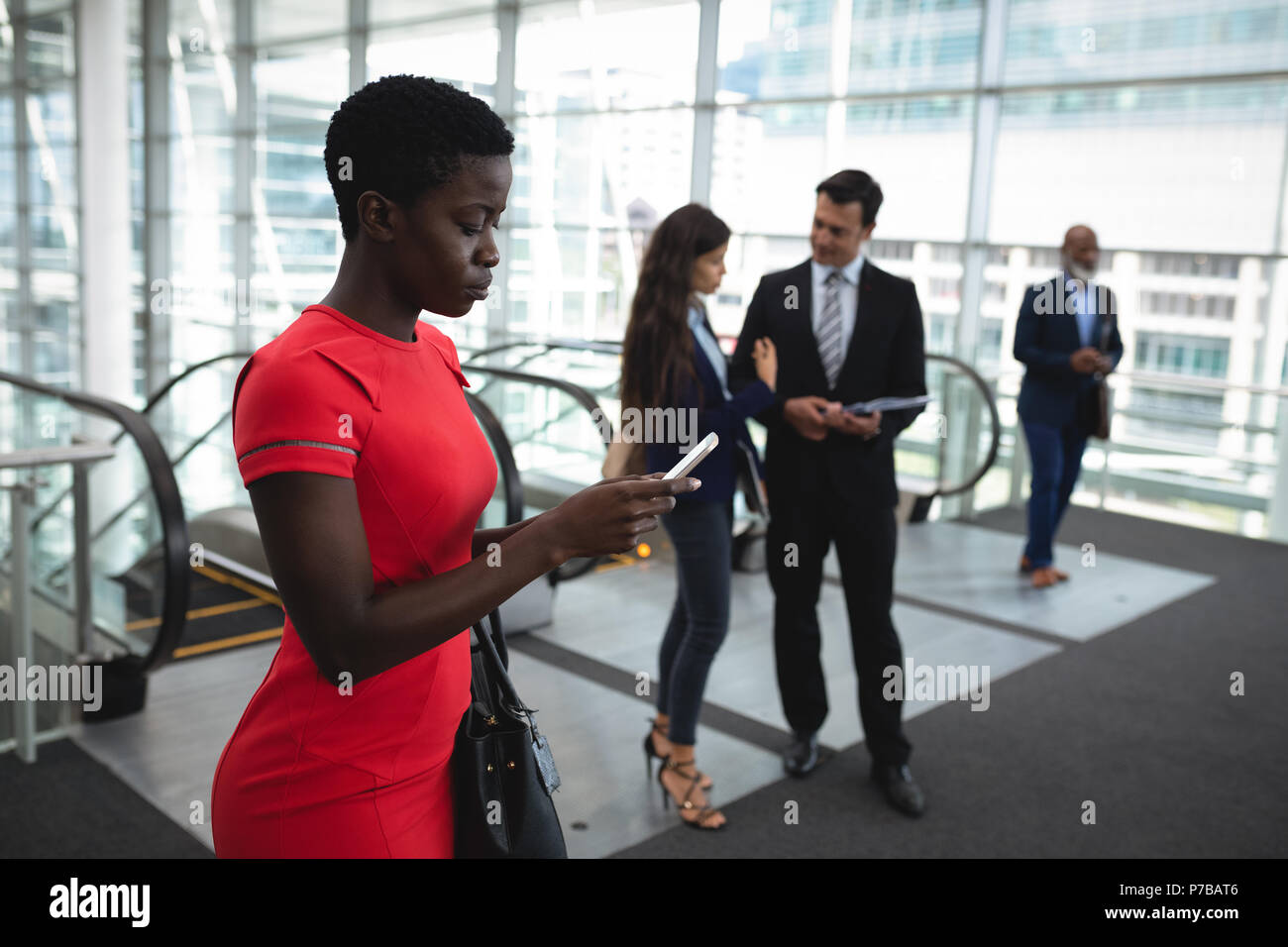 Businesswoman using her phone while colleagues are discussing Stock Photo