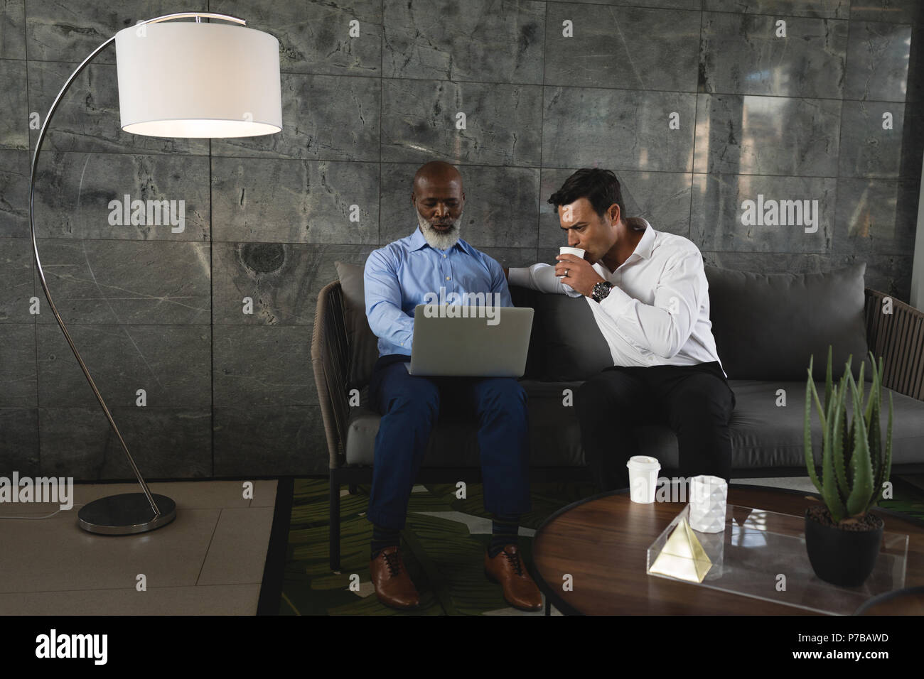 Businessmen having coffee and discussing over laptop Stock Photo