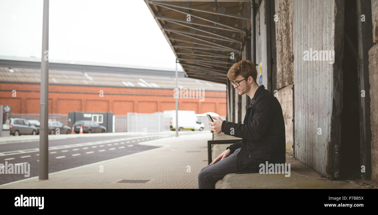 Man sitting by the pavement and using his mobile phone Stock Photo