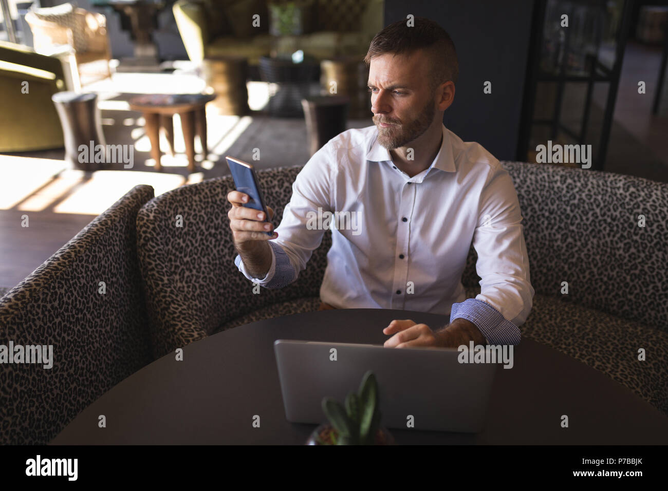 Businessman using phone while working on laptop in cafeteria Stock Photo