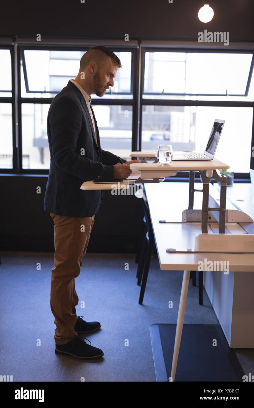 Businessman writing on notepad while using laptop Stock Photo