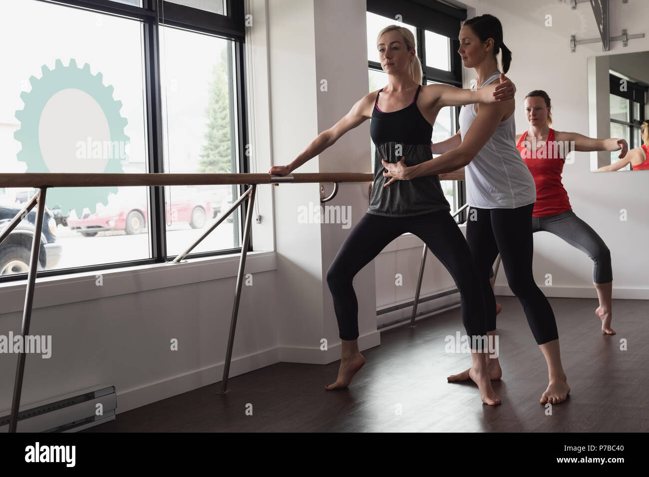 Trainer assisting young woman stretching on barre Stock Photo