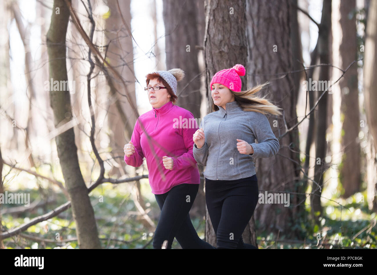 Mother and daughter wearing sportswear and running in forest at ...
