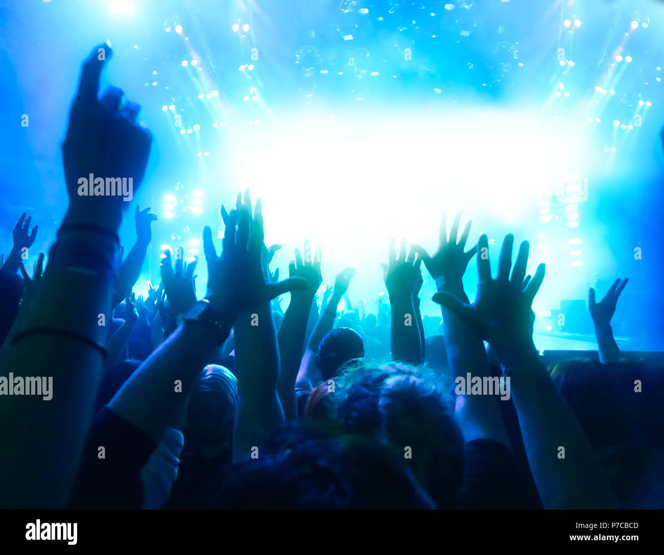 cheering crowd at rock concert in front of bright lights Stock Photo