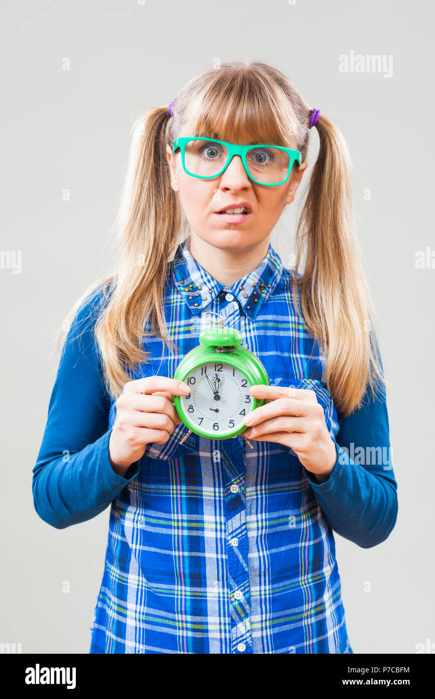 Studio shot portrait of nerdy woman who is holding clock that shows five to twelve time Stock