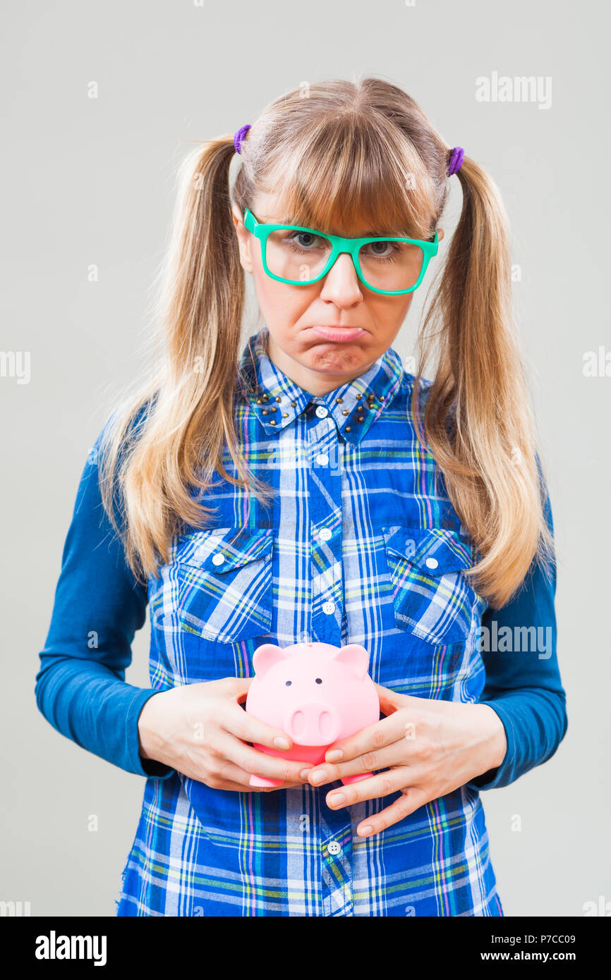 Studio shot portrait of sad nerdy woman who is holding empty piggy bang. Stock Photo