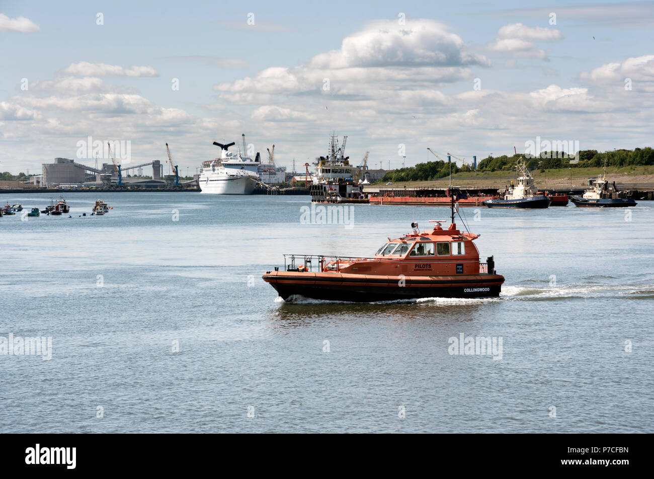 A pilot boat crosses the River Tyne, with a ship docked at the Ferry Port in the background, North Shields, Tyneside, UK Stock Photo