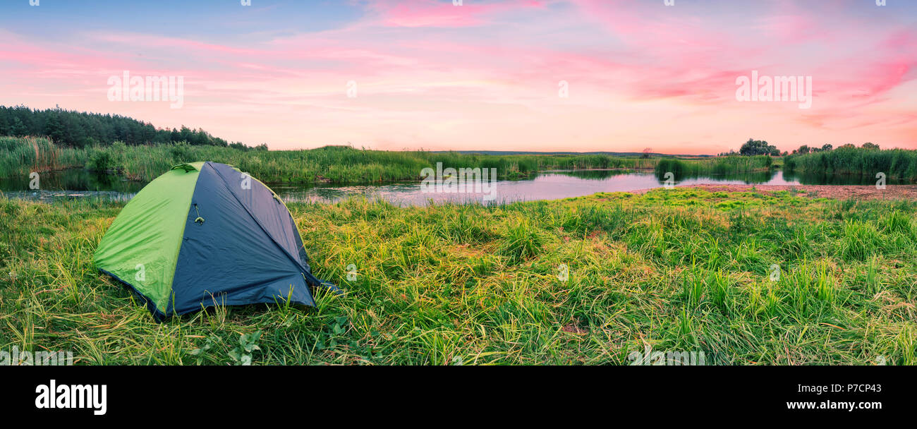 Green tourist tent on the river bank at dawn Stock Photo